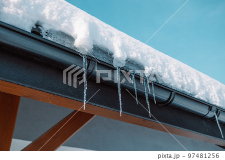 Sharp icicles and melted snow hanging from eaves of roof. Beautiful transparent icicles slowly gliding of a roof. 97481256