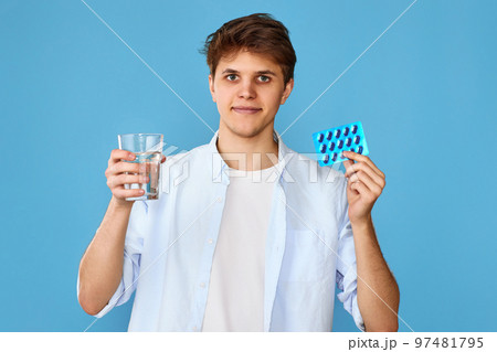 man holding pill and glass of water on blue background 97481795