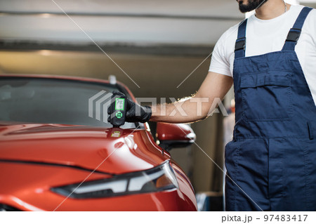 Closeup view of male hand, using film coating thickness gauge device to check car paint. 97483417