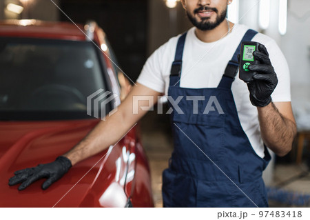 Cropped view of bearded young male inspector measuring paint cover thickness of the car body 97483418