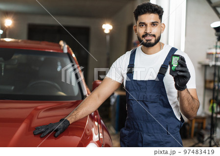 Bearded young male inspector measuring paint cover thickness of the car body at the vehicle service 97483419
