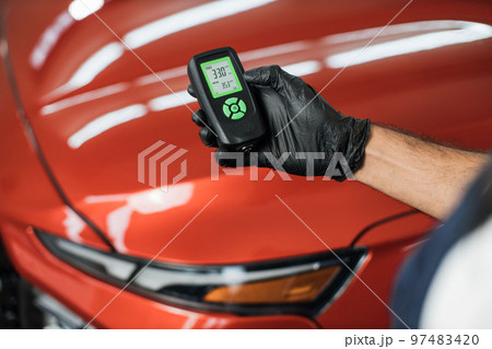 Closeup view of male hand, using film coating thickness gauge device to check car paint. 97483420