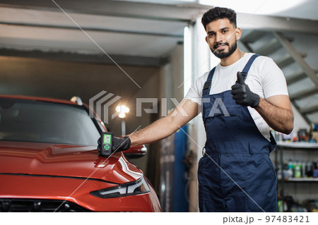 Professional service specialist testing thickness of the car paint in protective gloves. 97483421