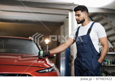 Professional service specialist testing thickness of the car paint in protective gloves. 97483422