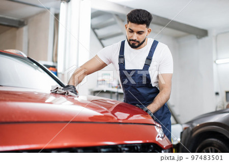 Young bearded male professional car wash worker in black rubber gloves, holding the gray microfiber Young bearded male professional car wash worker in black rubber gloves, holding the gray microfiber 97483501