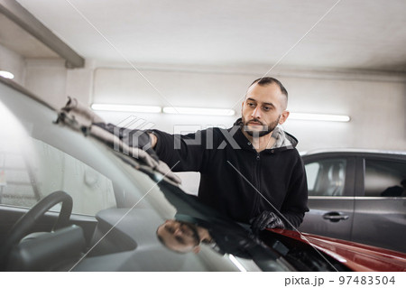 Young male car wash worker, wearing black gloves, wipes and polishes car windshield Young male car wash worker, wearing black gloves, wipes and polishes car windshield 97483504