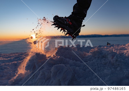 Man climbs a mountain peak in winter during sunrise. A shoe with spikes on - crampons.  97486165