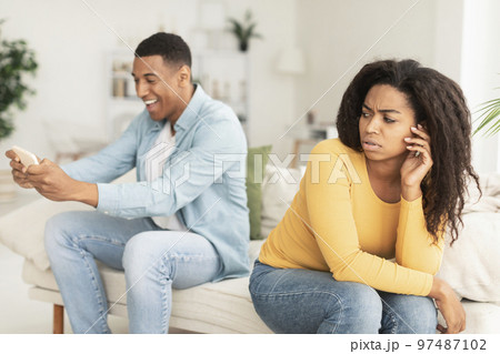 Sad young black wife look at husband, playing online game, chatting in social networks on smartphone 97487102