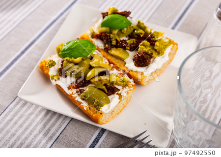 Slices of toasted bread with cream cheese, pickled olives and sun-dried tomatoes Slices of toasted bread with cream cheese, pickled olives and sun-dried tomatoes 97492550