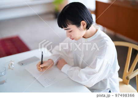 部屋でノートに書きものをする若い女性 97498366