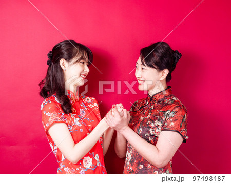 赤い背景に伝統的なチャイナドレスを着て微笑む若い娘と母のポートレート。 赤い背景に伝統的なチャイナドレスを着て微笑む若い娘と母のポートレート。 97498487
