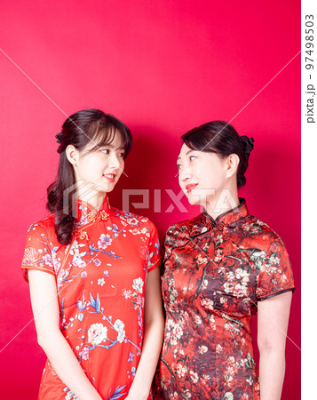 赤い背景に伝統的なチャイナドレスを着て微笑む若い娘と母のポートレート。 97498503