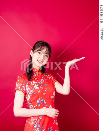 赤の背景に分離された紹介のジェスチャーで伝統的なチャイナ ドレスを着ているアジアの若い女性。 赤の背景に分離された紹介のジェスチャーで伝統的なチャイナ ドレスを着ているアジアの若い女性。 97498678