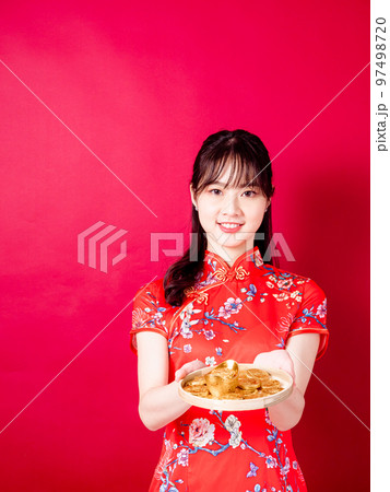 赤い背景に旧正月を祝うための金のインゴットを示す伝統的なチャイナドレスを着た幸せなアジアの若いアジア 97498720