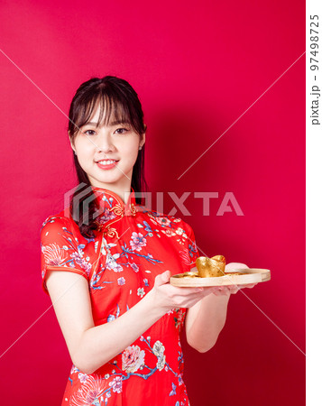 赤い背景に旧正月を祝うための金のインゴットを示す伝統的なチャイナドレスを着た幸せなアジアの若いアジア 97498725