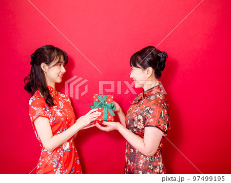 伝統的なチャイナ ドレスを身に着けている若い娘は、お母さんを祝福し、ギフト 97499195