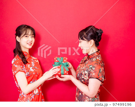 伝統的なチャイナ ドレスを身に着けている若い娘は、お母さんを祝福し、ギフト 97499196