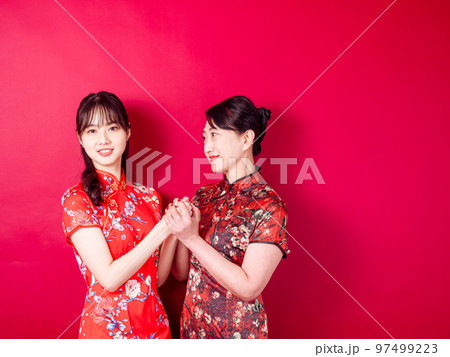 赤い背景に伝統的なチャイナドレスを着て微笑む若い娘と母のポートレート。 赤い背景に伝統的なチャイナドレスを着て微笑む若い娘と母のポートレート。 97499223