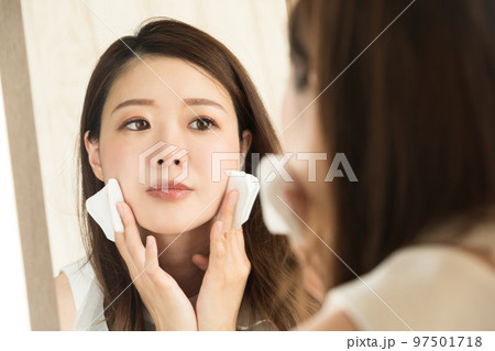 女性は鏡を見て、コットンを頬にあてている。 女性は鏡を見て、コットンを頬にあてている。 97501718
