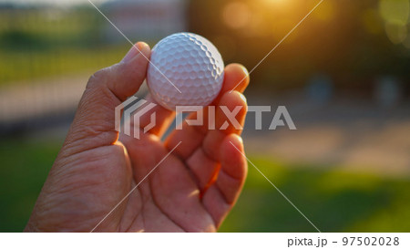 Hand hold golf ball with tee on course, golf course background 97502028