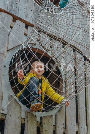 A child climbs up an alpine grid in a park on a playground on a hot summer day. children's playground in a public park, entertainment and recreation for children, mountaineering training. Child 97504169
