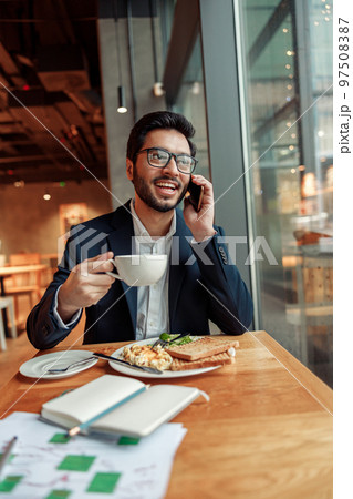 Happy indian businessman is talking phone with client during lunch time in cozy cafe Happy indian businessman is talking phone with client during lunch time in cozy cafe 97508387