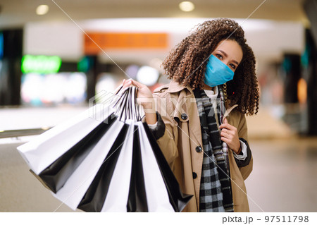 Young woman in protective medical mask with shopping bags 'near mall. Beautiful woman after shopping. 97511798
