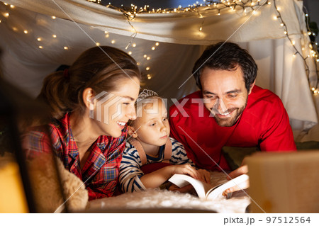 Smiling family, mother, father and daughter lying inside self-made hut, tentunder Christmas lights and spending time together 97512564