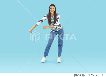 Young woman in casual clothes doing funny floss dancing move on blue studio background Young woman in casual clothes doing funny floss dancing move on blue studio background 97512964