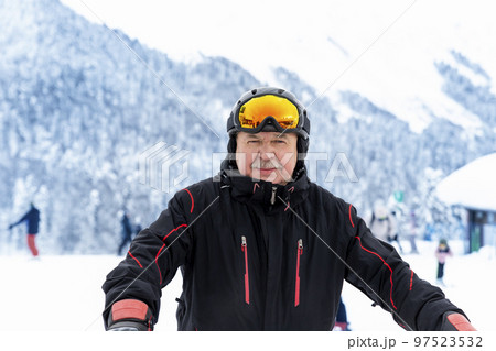 Active senior experienced mature old person in ski helmet, goggles and black suit stand against scenic panorama peak enjoy cold extreme sport activities. Man on mountains forest winter background 97523532