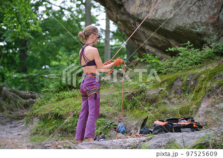 Woman belays her partner climber with belaying device and rope. Climber's helper holding equipment for rock mountaineering security. Woman belays her partner climber with belaying device and rope. Climber's helper holding equipment for rock mountaineering security. 97525609