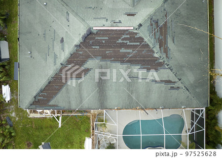 Wind damaged house roof with missing asphalt shingles after hurricane Ian in Florida. Repair of home rooftop concept 97525628