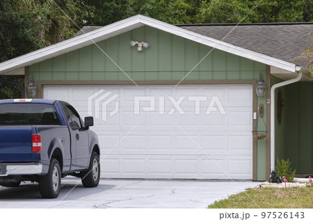 Vehicle parked in front of wide garage double door on paved driveway of typical contemporary american home 97526143