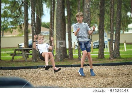 Two young teenage children, girl and boy playing on swings together outdoors on bright sunny vacations day 97526148