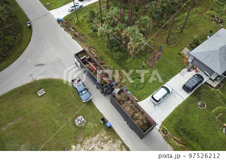Top view of Hurricane Ian special aftermath recovery dump truck picking up tree branches debris from Florida rural streets. Dealing with consequences of natural disaster Top view of Hurricane Ian special aftermath recovery dump truck picking up tree branches debris from Florida rural streets. Dealing with consequences of natural disaster 97526212