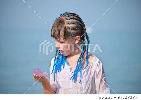 Funny cute girl looking surprised at pink transparent jellyfish in palm of her hand, bright blue sky background 97527377