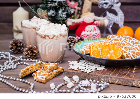 Christmas cookies and dried mandarin slices in a plate and hot cocoa with marshmallows in glasses on the table in Christmas decorations 97527600