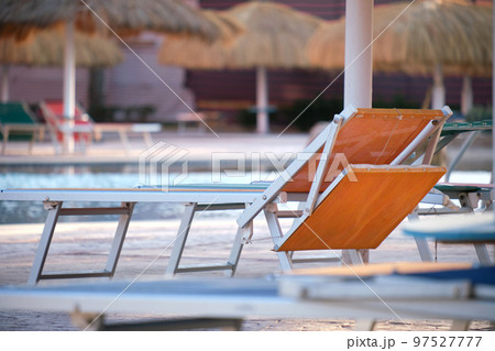 Empty deck chairs under straw shade umbrellas on swimming pool side in tropical resort. Summer vacations and getaway concept 97527777