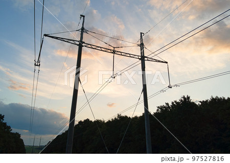 Dark silhouette of high voltage tower with electric power lines at sunrise. 97527816
