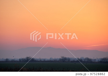 Beautiful evening panoramic landscape with bright setting sun over distant mountain peaks at sunset 97528862