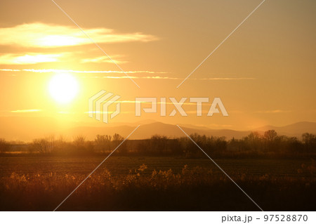Beautiful evening panoramic landscape with bright setting sun over distant mountain peaks and asphalt road in front at sunset 97528870
