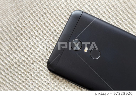 Back side of black cellphone isolated with security thumb fingerprint scanning device, camera and flash lighting on light cloth copy space background. Modern technology and smartphone design concept. 97528926