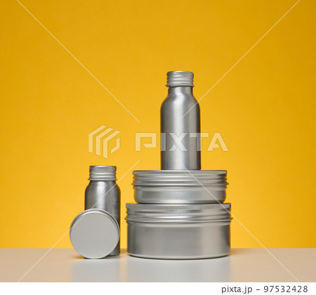 Empty silver metal bottle for cosmetics on white table, yellow background. Packaging for cream Empty silver metal bottle for cosmetics on white table, yellow background. Packaging for cream 97532428