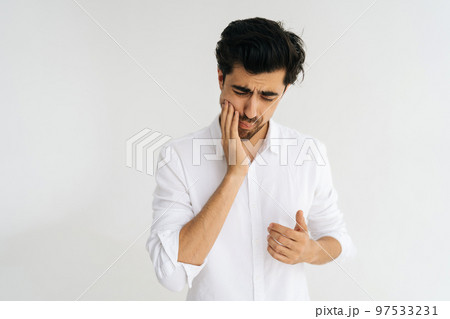 Medium shot studio portrait of unhappy man with closed eyes suffering from severe toothache, touching jaw with fingers trying to ease strong tooth pain standing on white isolated background. 97533231