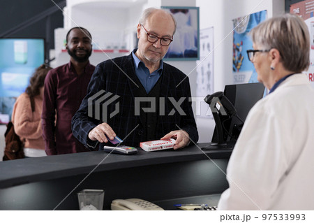 Senior client paying disease medications with credit card using payment terminal during health care shopping session in pharmacy. Old customer buying supplements, vitamins to help cure illness Senior client paying disease medications with credit card using payment terminal during health care shopping session in pharmacy. Old customer buying supplements, vitamins to help cure illness 97533993