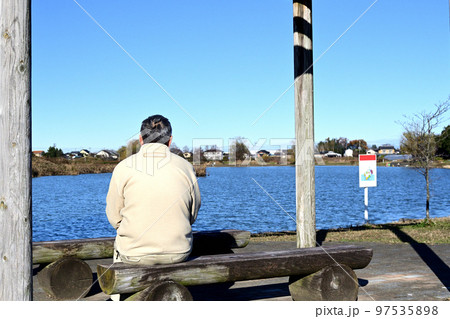 冬の日を背中に浴びて公園のベンチでのんびりと日向ぼっこする老人 冬の日を背中に浴びて公園のベンチでのんびりと日向ぼっこする老人 97535898