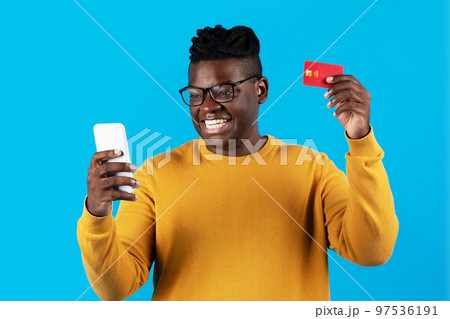Cheerful Young Black Man Using Smartphone And Credit Card For Online Shopping 97536191