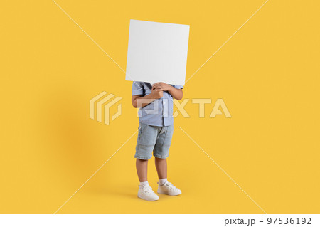 Kids mood. Adorable unrecognizable little boy posing with blank sheet of paper near face, orange background, empty space 97536192
