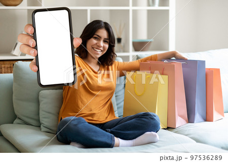 Mobile Ad. Smiling Middle Eastern Female Demonstrating Blank Smartphone And Shopping Bags 97536289
