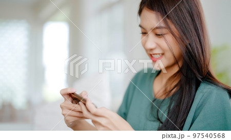 Happy young asian woman relax on comfortable couch at home texting messaging on smartphone 97540568